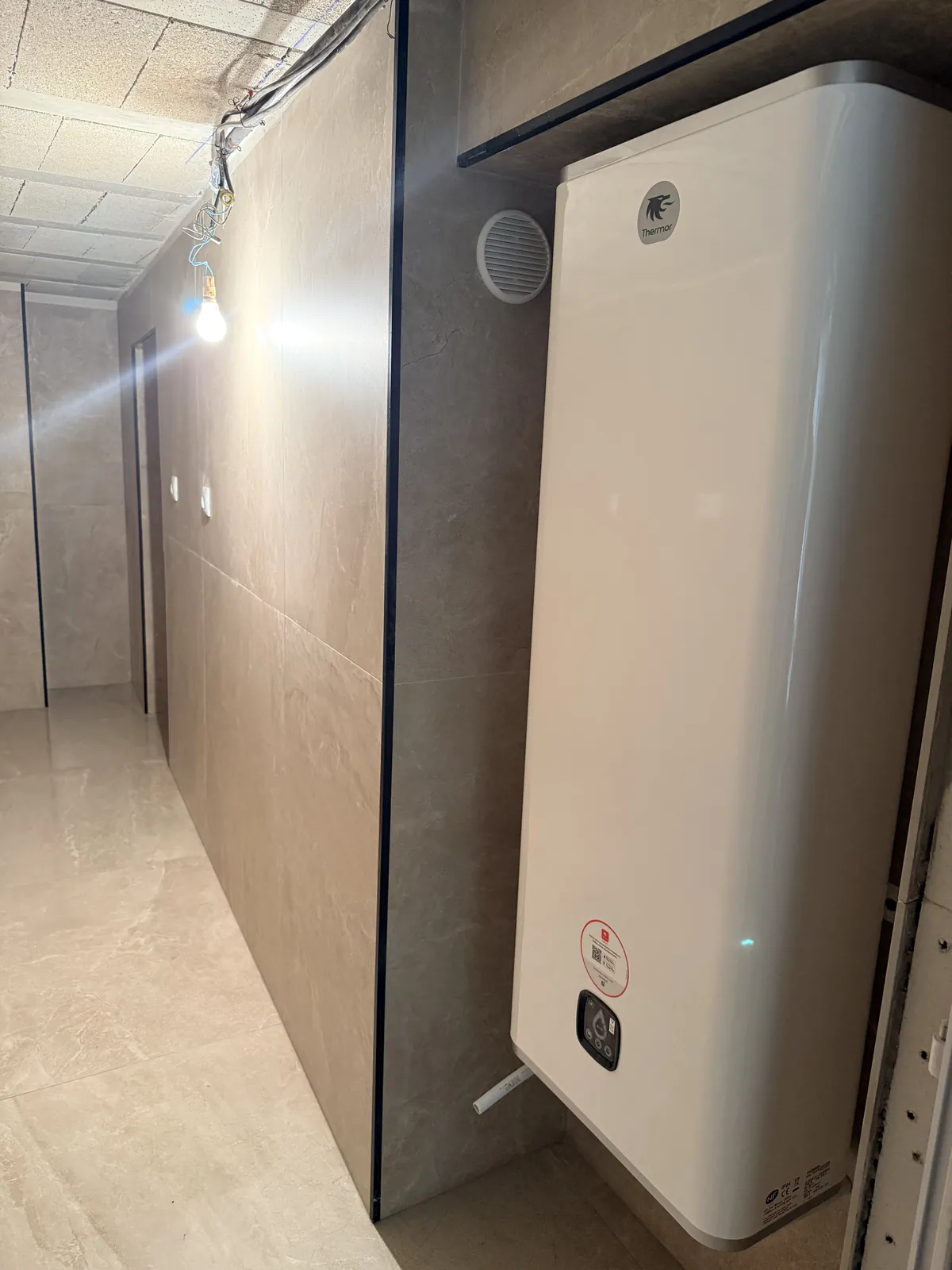 Le chauffe-eau électrique installé, avec la grille de ventilation au-dessus.